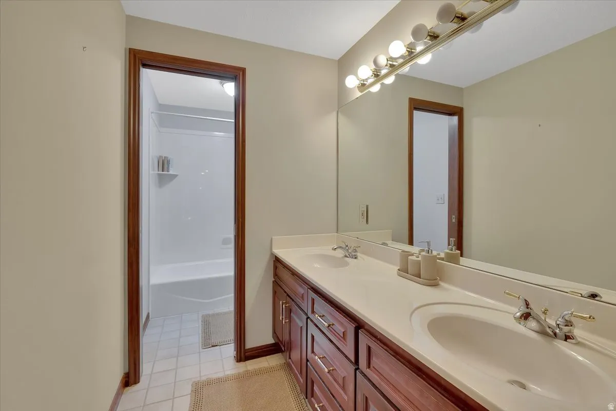 Bathroom featuring a double vanity with integrated sinks, a wide mirror, and a wall-mounted light fixture