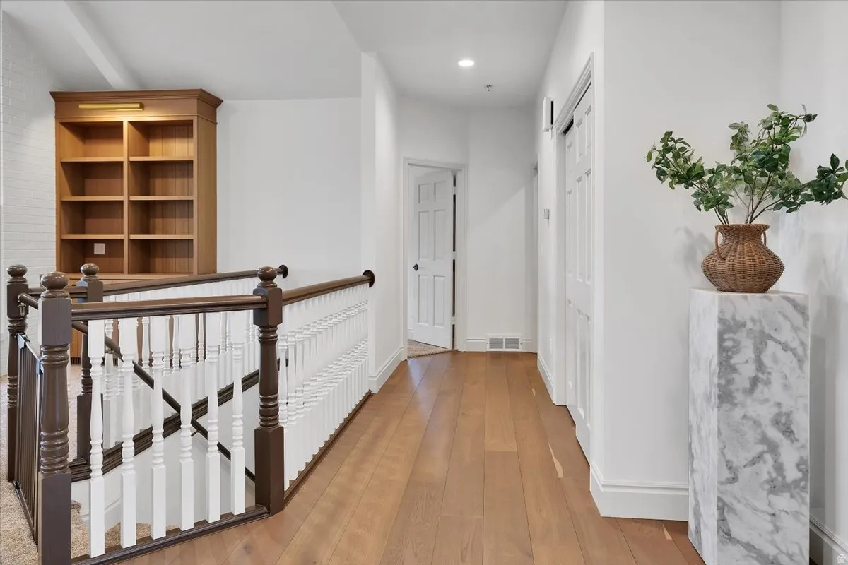 Hardwood flooring extending through a bright hallway featuring a built-in wooden bookcase with integrated lighting