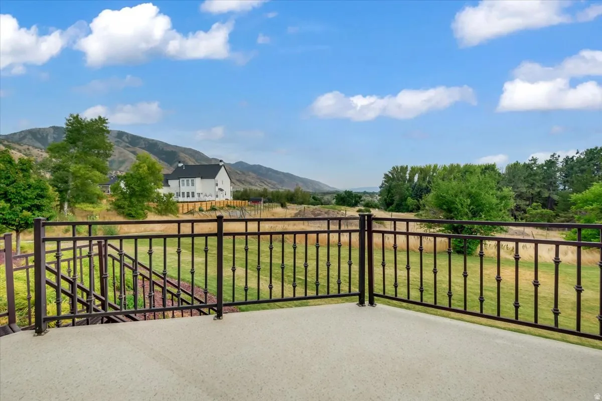 Outdoor deck with a concrete surface and a decorative metal railing, overlooking a expansive green landscape with distant mountains