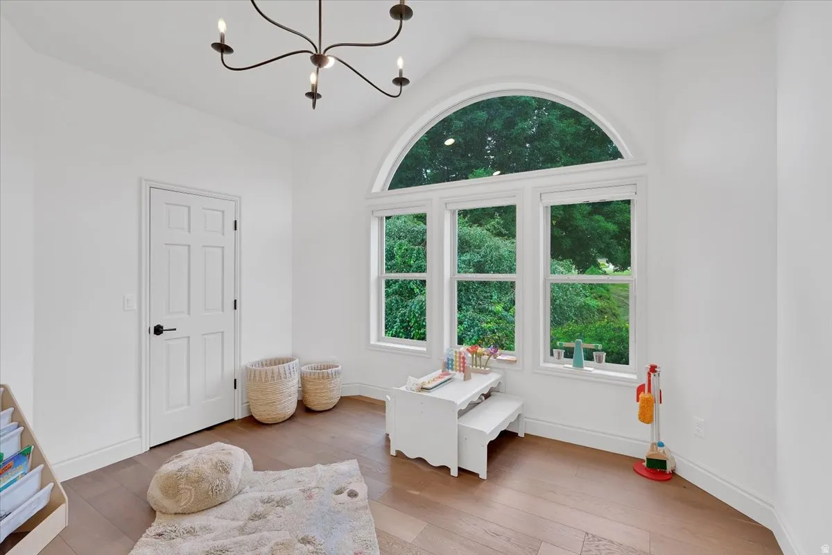 Vaulted ceiling room featuring a large arched window, three rectangular windows, a six-panel interior door with black hardware, wood-finish flooring, and a multi-arm chandelier
