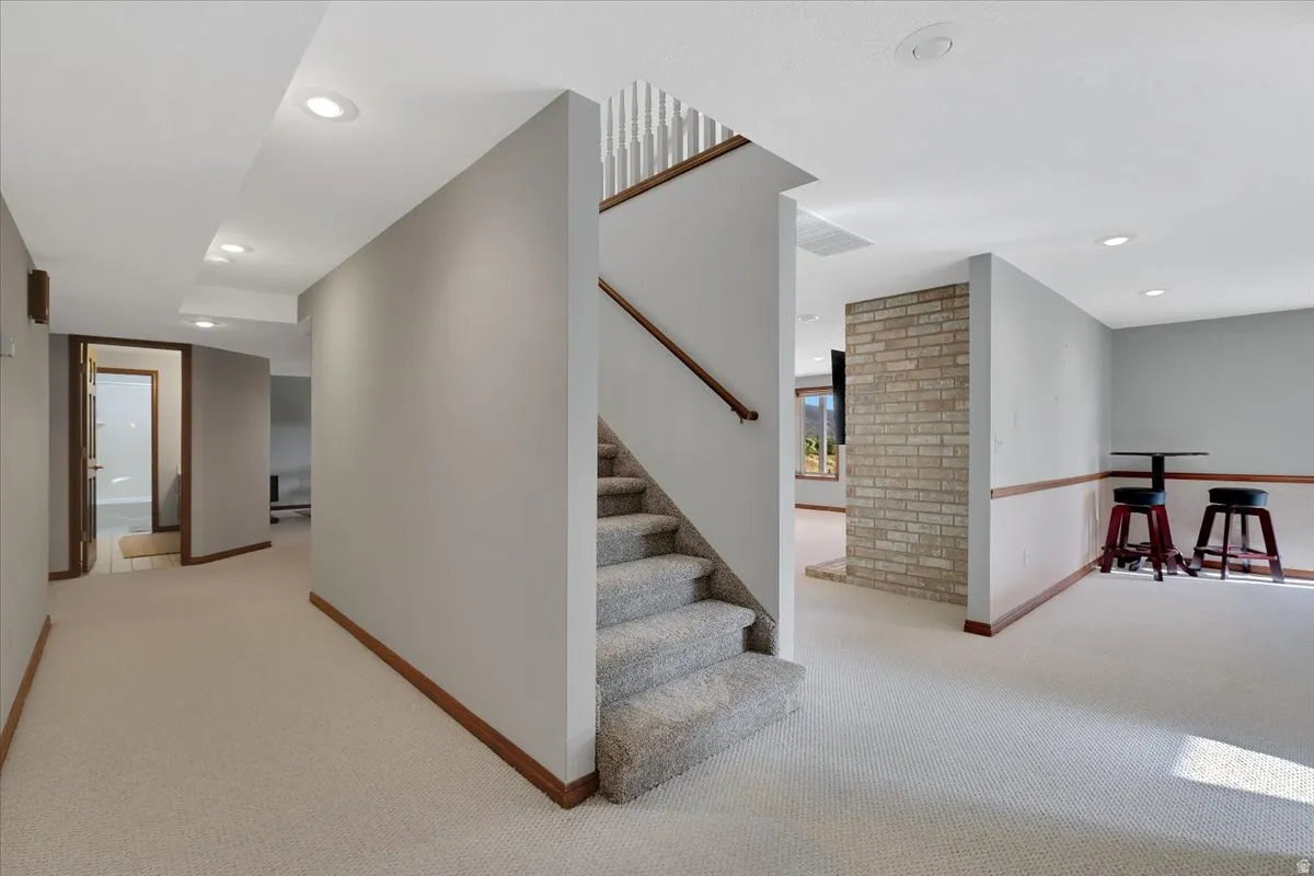 Finished basement featuring light gray walls, recessed lighting, and a staircase with light-colored carpet and a wood handrail