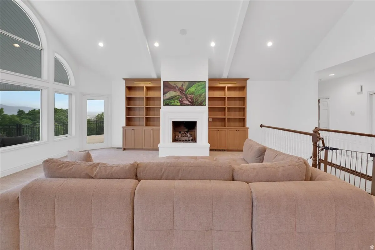 Spacious living area featuring a prominent fireplace with mantel, built-in shelving, vaulted ceilings, and large arched windows