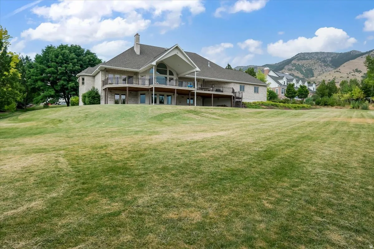 Expansive rear lawn featuring a two-story residence with a stone and stucco exterior, multiple decks, and a prominent gable with arched window framing