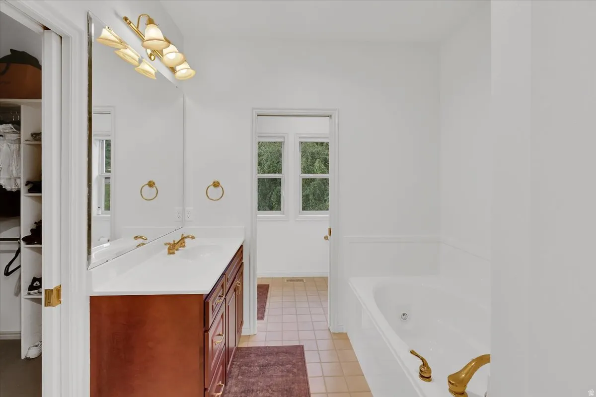 Bathroom featuring a double vanity with wood-finish cabinetry, a large mirror, and a built-in jetted tub