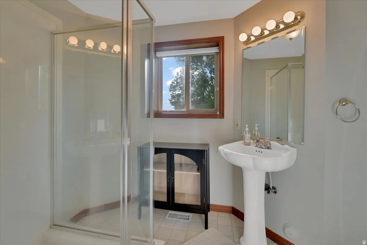 Three-quarter bathroom featuring a glass-enclosed shower, pedestal sink, wall-mounted mirror, and wood-trimmed window