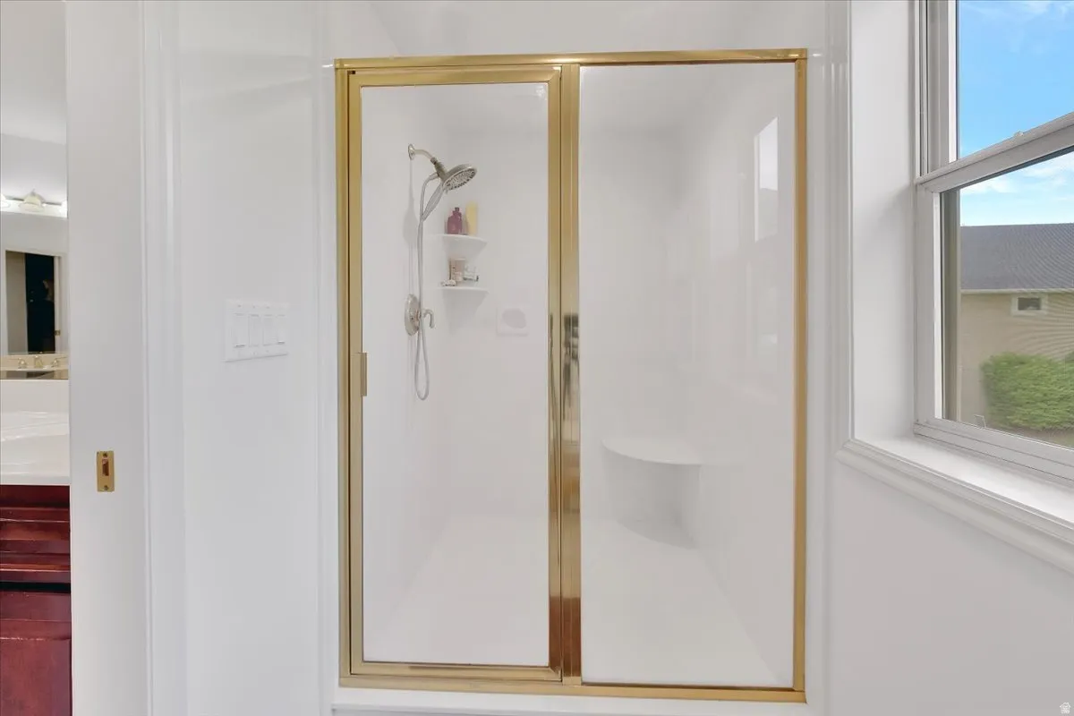 Enclosed shower with gold-finish frame, integrated shelving, and built-in bench