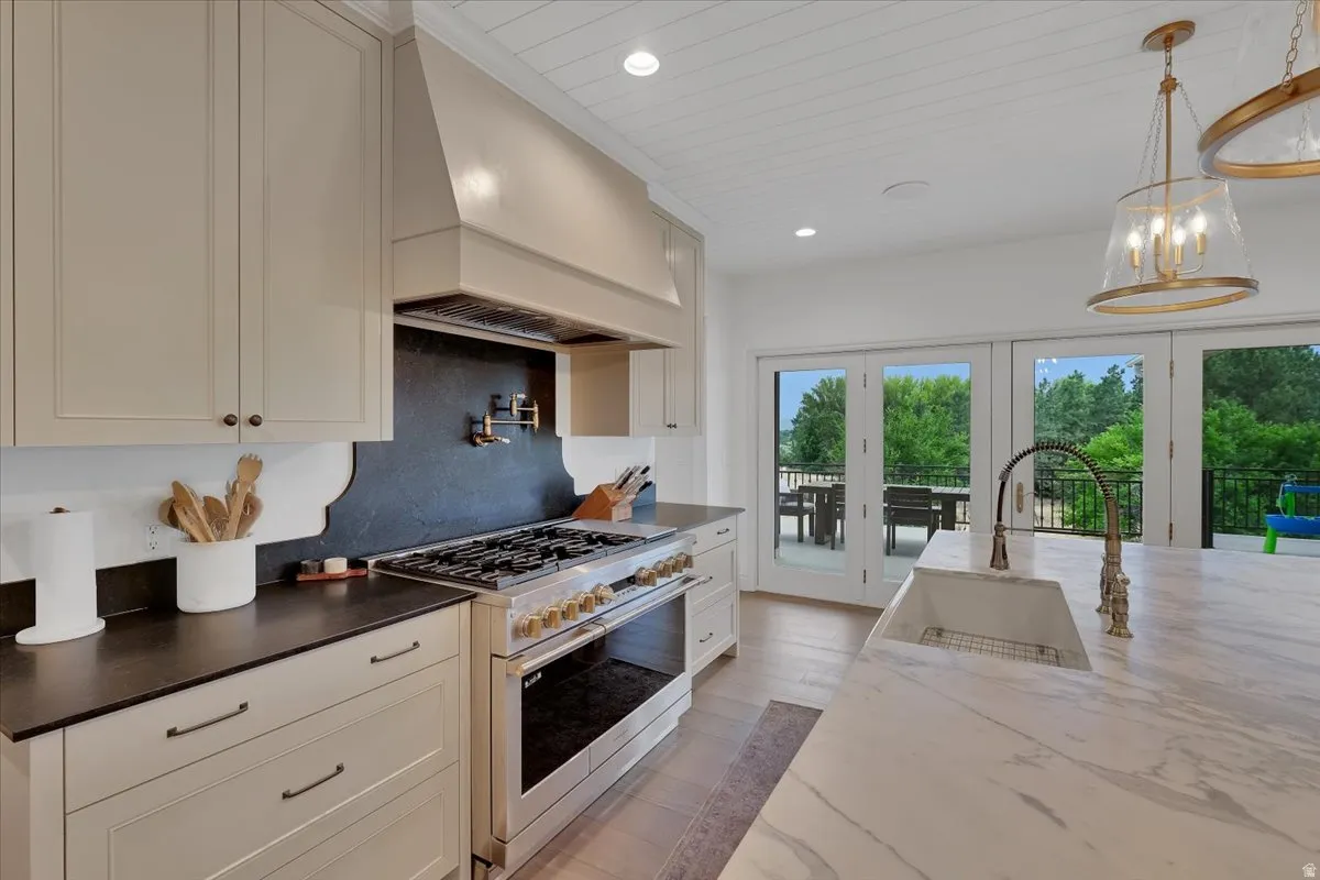 Gourmet kitchen featuring a large central island with an integrated sink, professional-grade range, custom range hood, and light-toned cabinetry