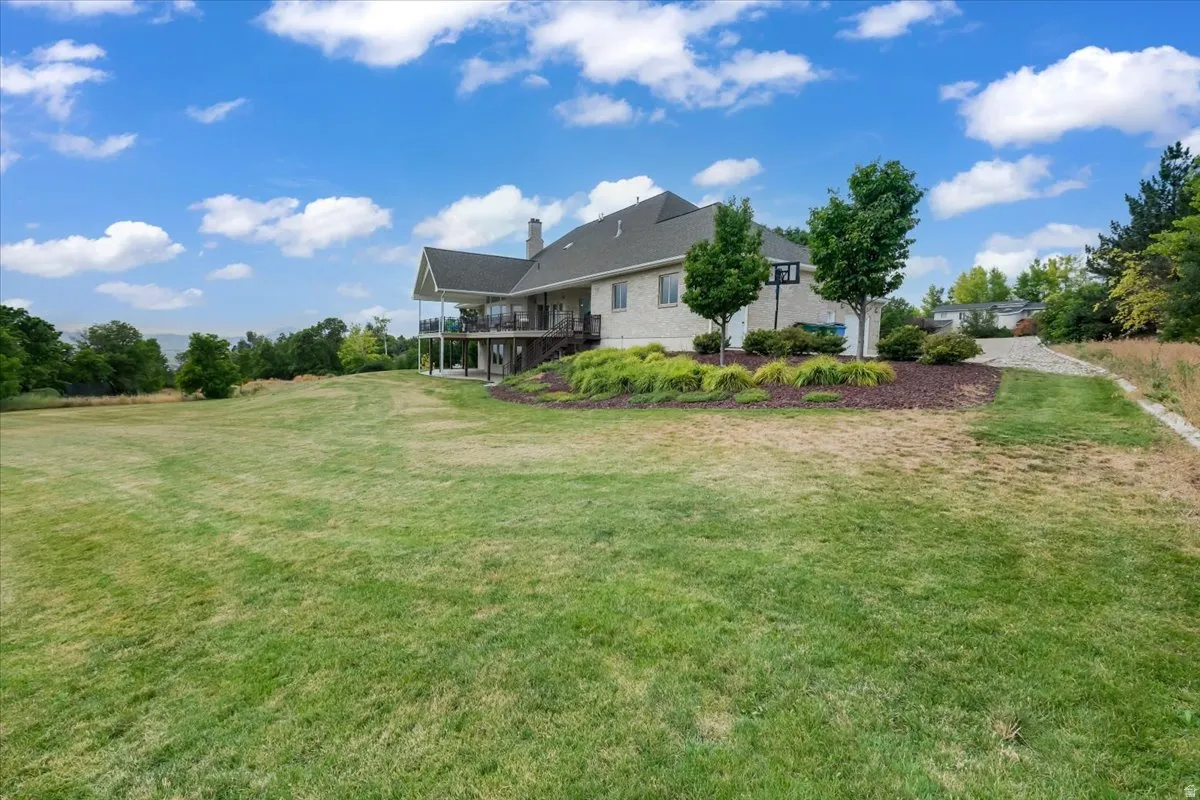 Expansive green space featuring a large grassy area, a multi-level dwelling with a covered balcony, and mature trees