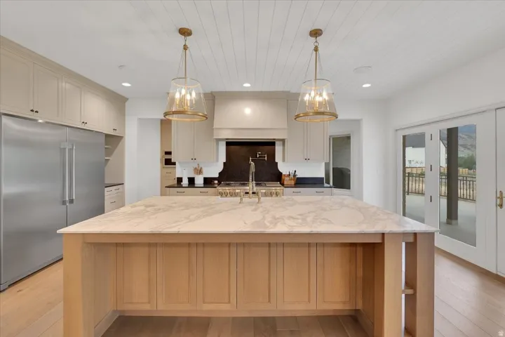 Gourmet kitchen featuring a substantial wood island with a substantial stone countertop, stainless steel refrigerator, white cabinetry, brass pendant lighting, and light wood-finish flooring