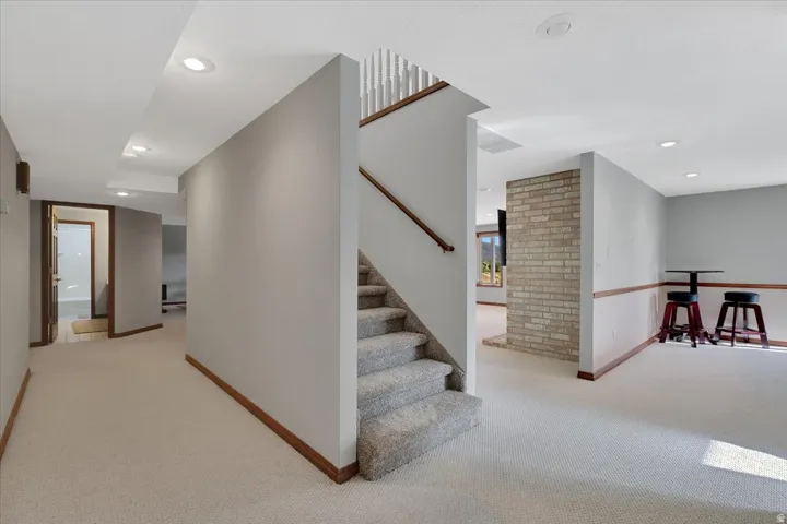 Finished basement featuring light gray walls, recessed lighting, and a staircase with light-colored carpet and a wood handrail