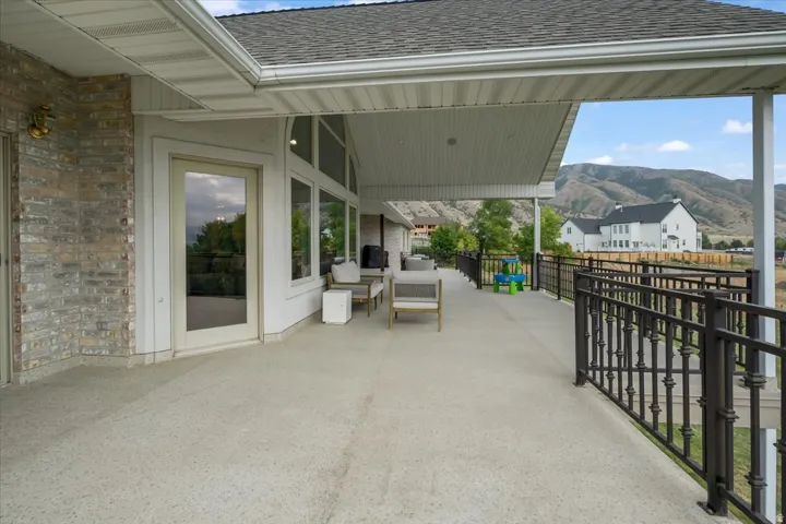 Spacious covered patio featuring a textured concrete surface, white trim, and a decorative metal railing