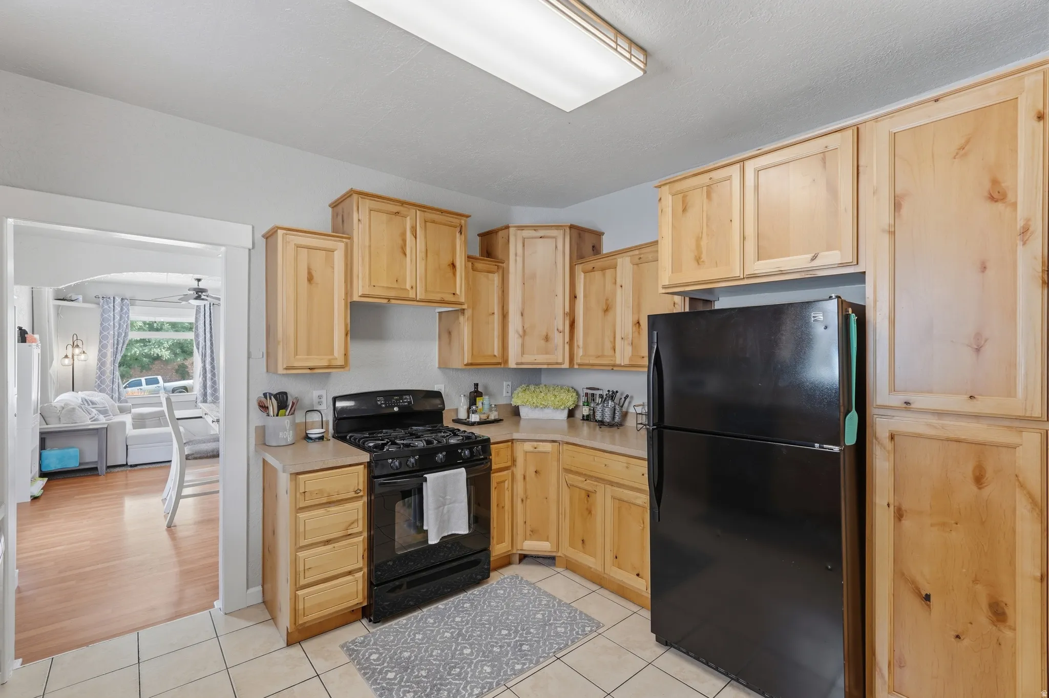 Kitchen featuring wood cabinetry, black appliances, light countertops, and tile flooring