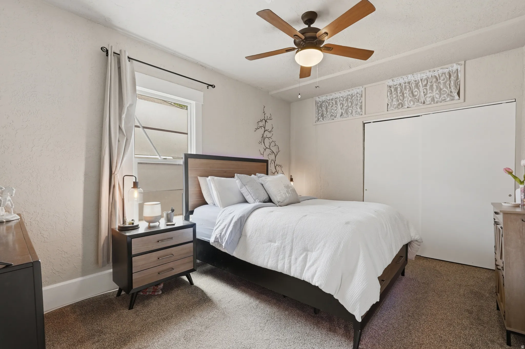 Bedroom featuring textured walls, a ceiling fan with light fixture, a window with trim, and white sliding closet doors