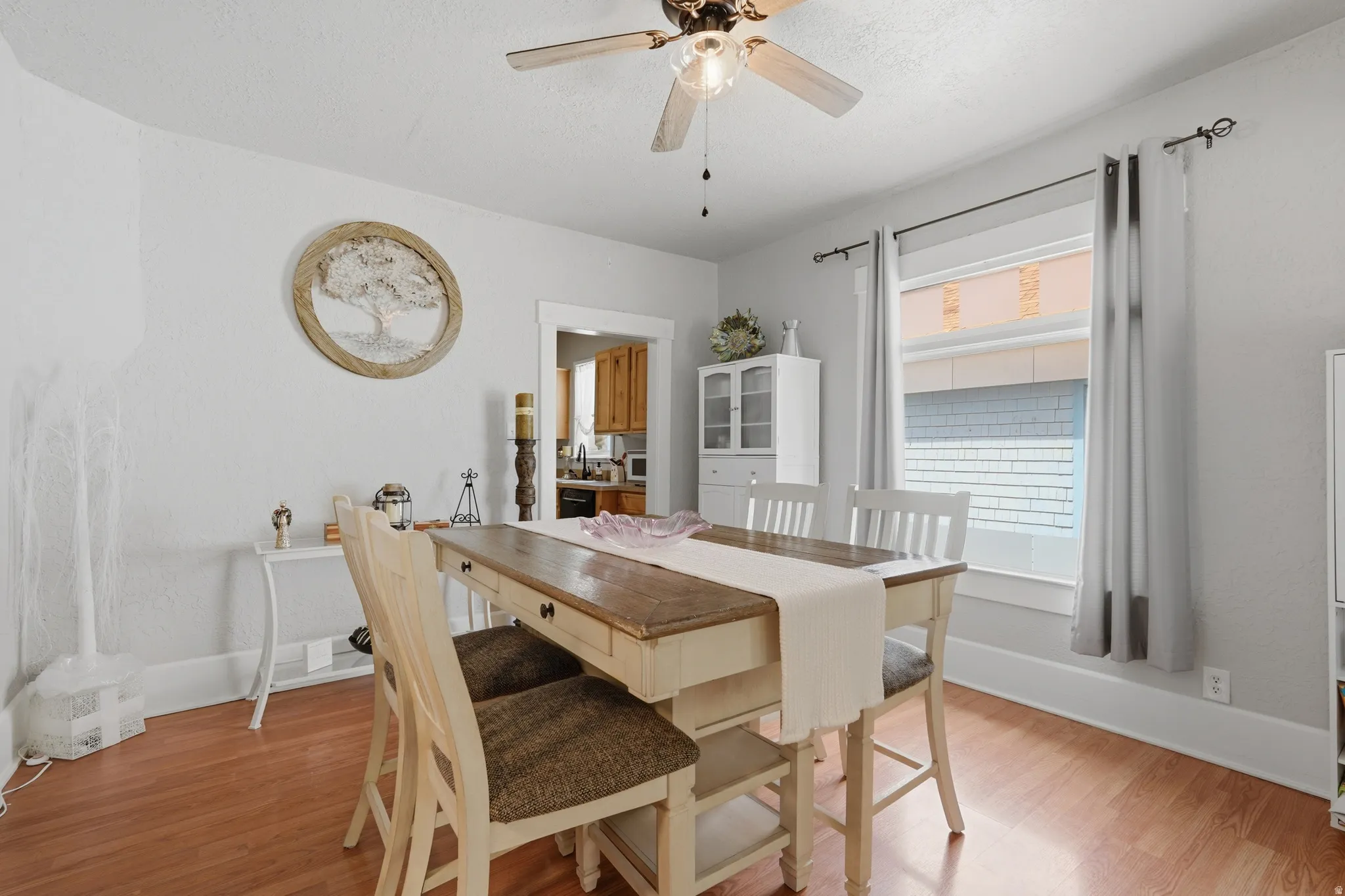 Dining area featuring wood-finish flooring, a ceiling fan with light fixture, light gray walls, and a large window with white trim