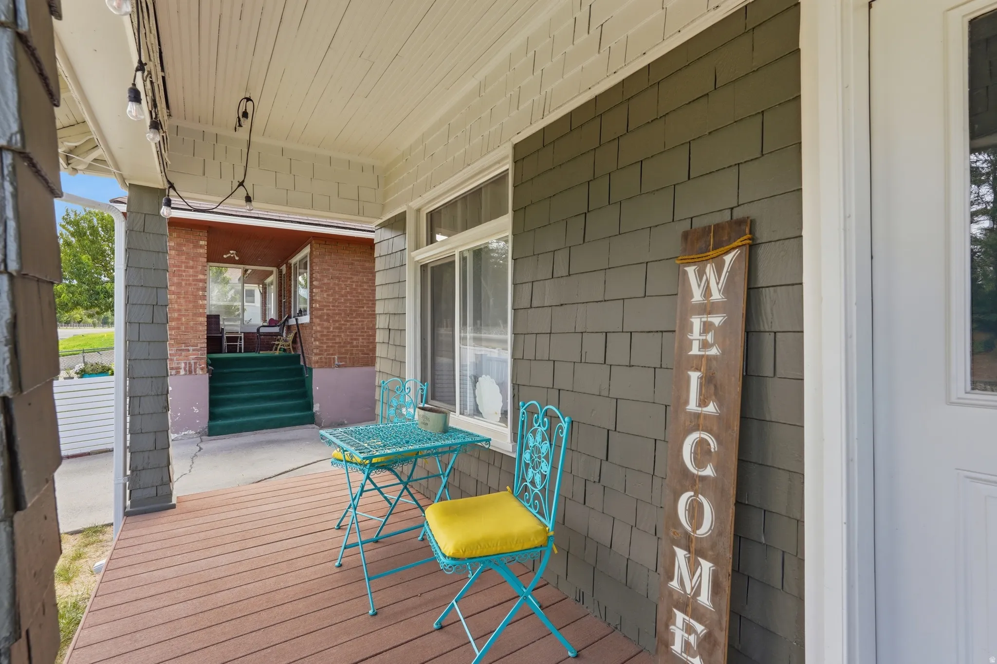 Covered front porch featuring wood-finish flooring, shake siding, and string lighting