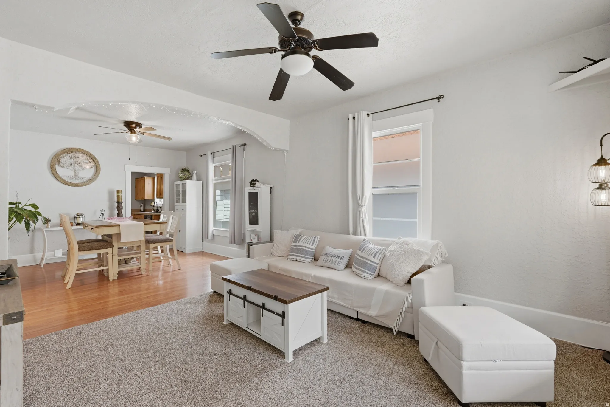 Spacious living area featuring light gray walls, a ceiling fan with integrated lighting, and a large window with white trim
