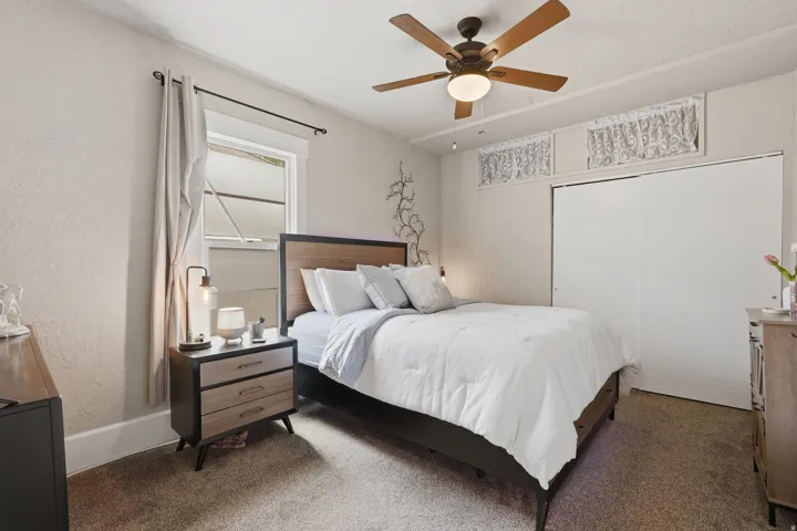 Bedroom featuring textured walls, a ceiling fan with light fixture, a window with trim, and white sliding closet doors
