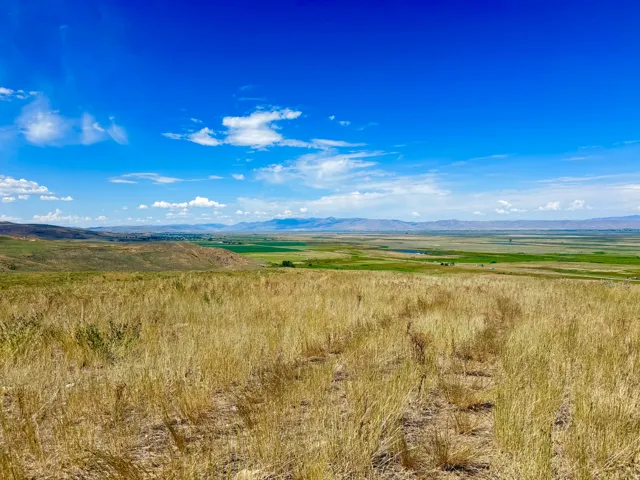 Expansive natural landscape featuring rolling hills and distant mountains under a clear blue sky