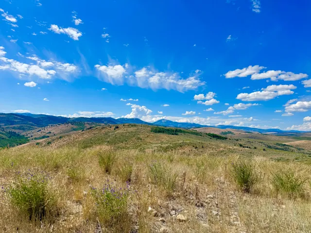 Expansive natural landscape featuring rolling hills, varied topography, and distant mountain ranges under a clear blue sky