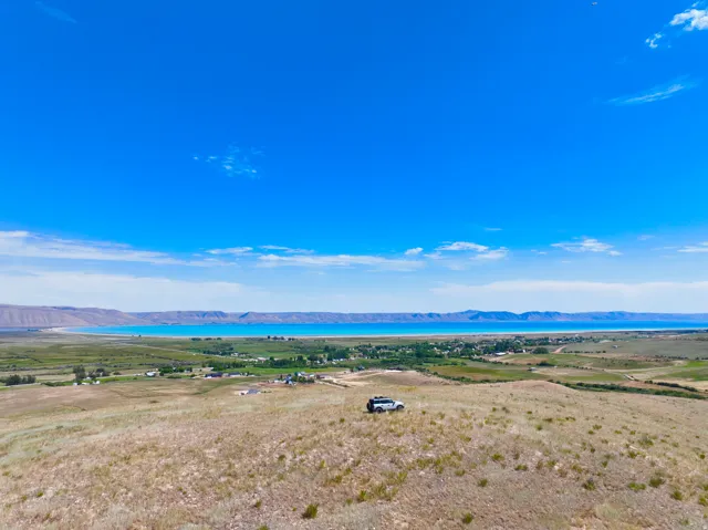 Expansive rural landscape featuring a large body of water, distant mountains, and a clear blue sky