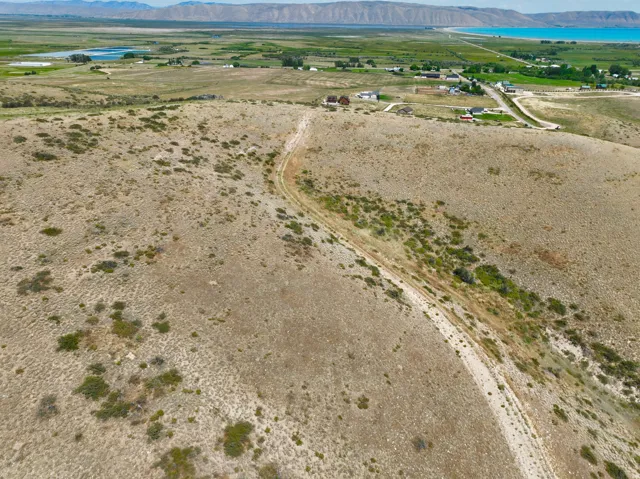 Expansive terrain featuring natural ground cover, distant mountains, a body of water, and scattered buildings