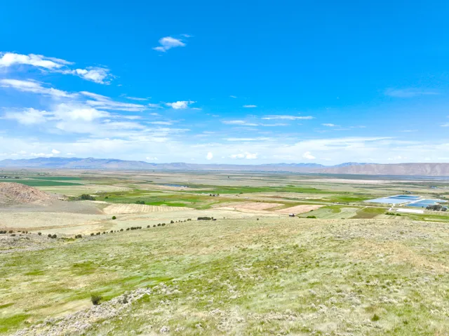 Expansive landscape featuring rolling hills and distant mountains under a clear blue sky with scattered clouds