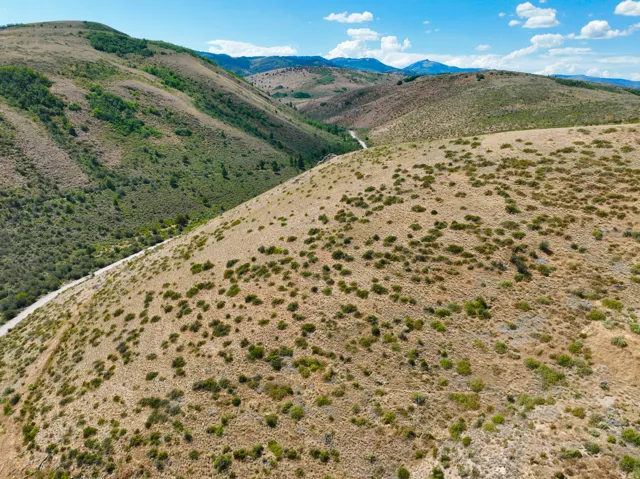 Expansive mountainous terrain featuring natural vegetation, visible slopes, and a distant winding road