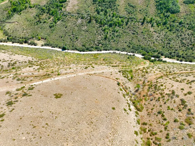 Expansive rural landscape featuring a winding dirt road, natural vegetation, and a mountainous backdrop