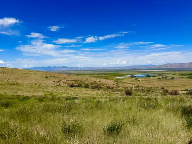 Expansive landscape showcasing rolling hills and a distant body of water under a clear blue sky