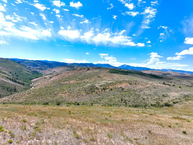 Expansive natural landscape with rolling hills, distant mountains, and a visible stream