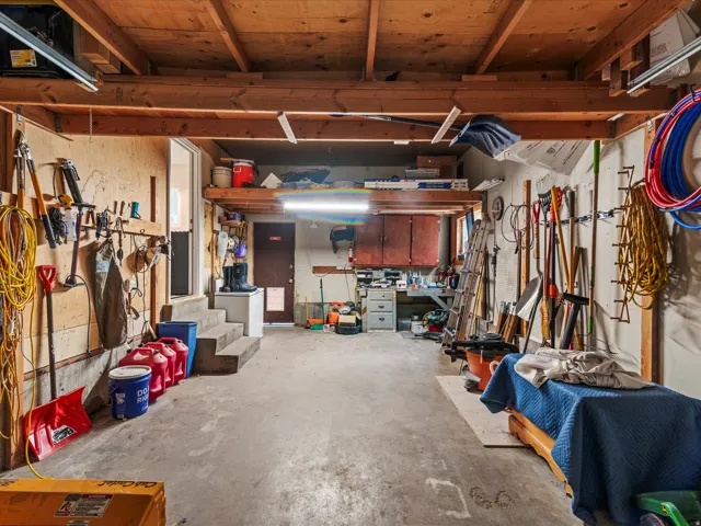 Spacious garage featuring exposed wood beam ceiling, concrete flooring, ample wall storage, and built-in shelving with cabinetry
