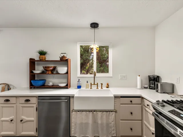 Kitchen featuring a white farmhouse sink with a gold-finish faucet, under-sink curtain, and a window with a black pendant light fixture