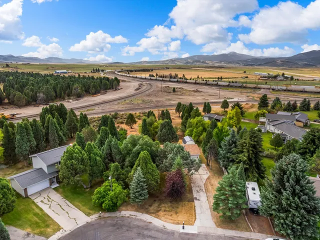 Expansive rural landscape featuring a residential area with mature trees, a distant railway line, and mountain ranges