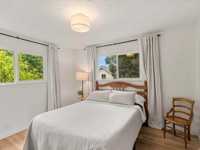 Bedroom featuring wood-finish flooring, white walls, and multiple windows with white trim
