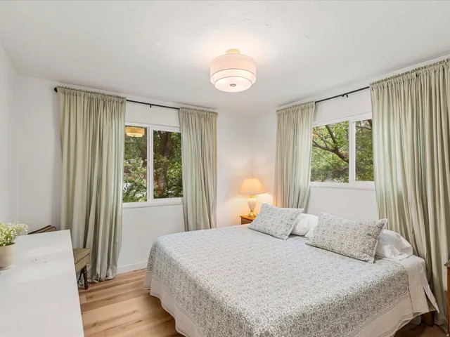 Dual windows with exterior tree canopy, wood-finish flooring, white walls, and a ceiling-mounted light fixture