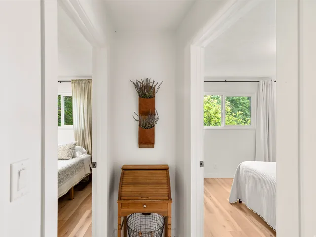 Bright hallway featuring a built-in wooden desk with a roll-top and two bedrooms with wood-finish flooring