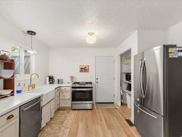 Kitchen featuring wood-finish flooring, white cabinetry with brass hardware, a farmhouse sink with a gold-tone faucet, stainless steel appliances, and a built-in pantry