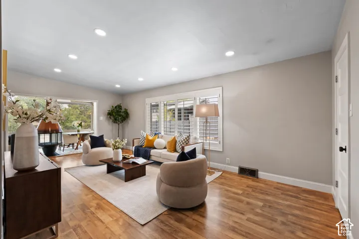 Spacious living area featuring wood-finish flooring, recessed lighting, and large windows with plantation shutters