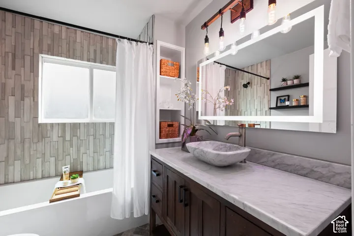 Bathroom featuring a dark wood-finish vanity with a stone vessel sink, a large back-lit mirror, and a wall-mounted faucet