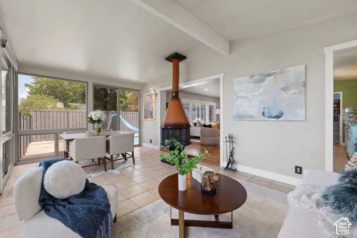 Sunroom featuring a freestanding fireplace, tile flooring, and exposed ceiling beams
