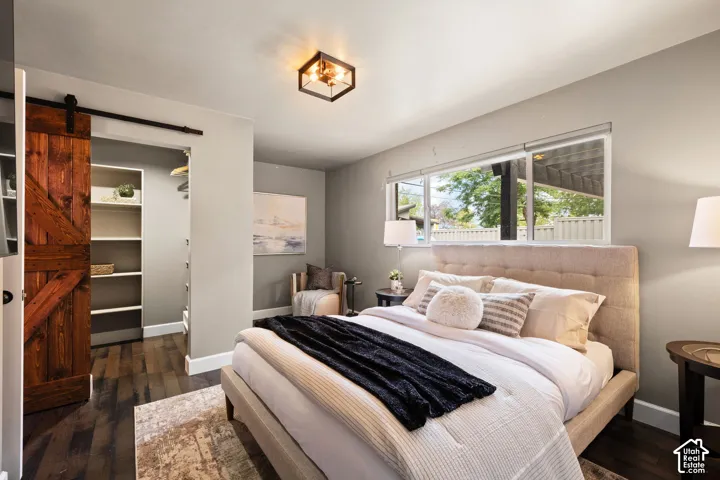 Bedroom featuring wood-finish flooring and a barn door entry to a custom built-in closet with shelving