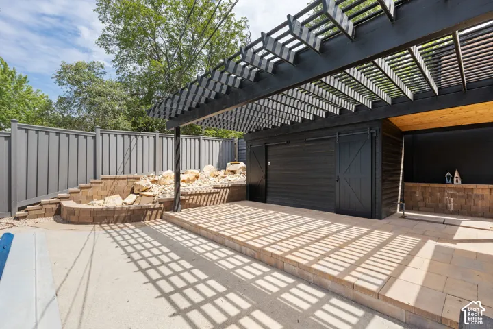 Custom patio featuring a black pergola, built-in stone landscaping, and a black storage shed with barn doors