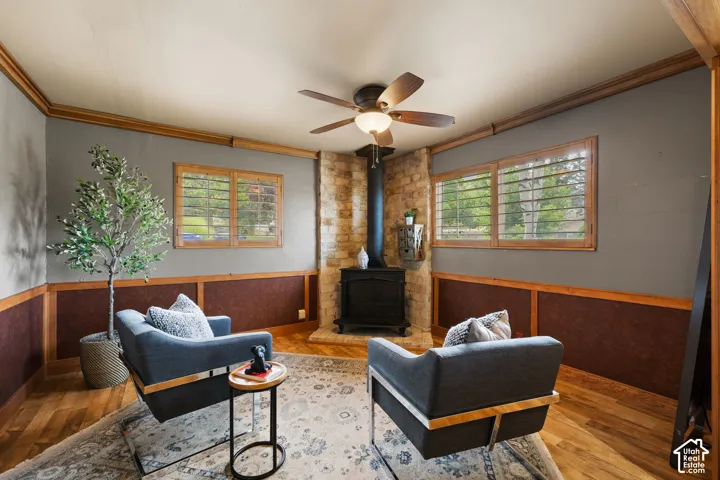 Inviting room featuring a stone-clad fireplace with a black wood-burning stove, wood-finish flooring, and two large windows with wooden plantation shutters