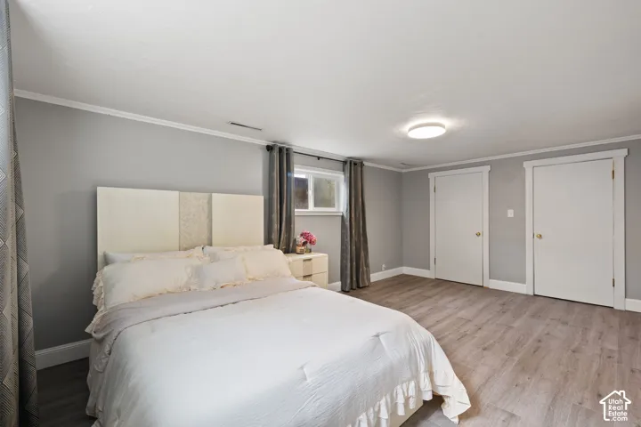 Bedroom with light gray walls, white trim, and wood-finish flooring
