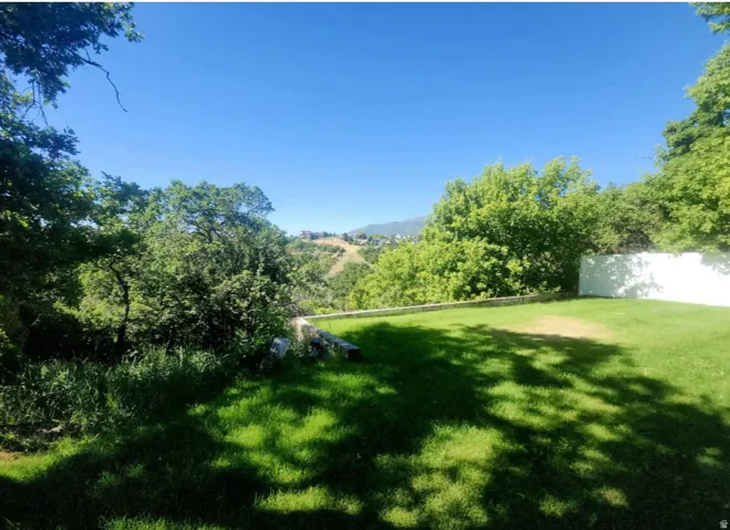 Expansive backyard featuring a green lawn, mature trees, and a distant mountain panorama