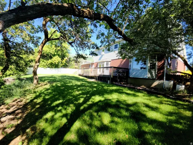 Spacious backyard featuring a large grassy area, mature trees, a multi-level wood deck, and partial fencing