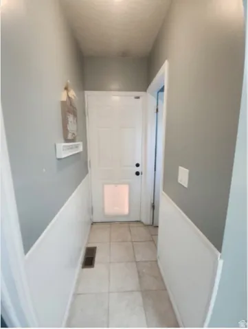 Back yard Entrance  featuring light neutral wall paint with white wainscoting, a paneled door, and square tile flooring