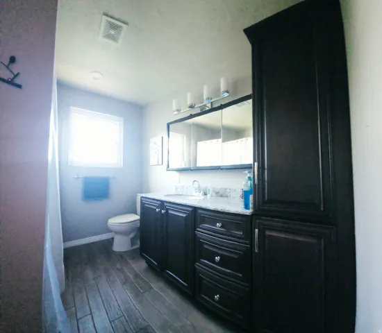 For upstairs bedroom 2&3 the full Bathroom featuring dark wood-finish cabinetry with a light-toned countertop, wood-finish flooring, a wall-mounted medicine cabinet with integrated lighting, and a window