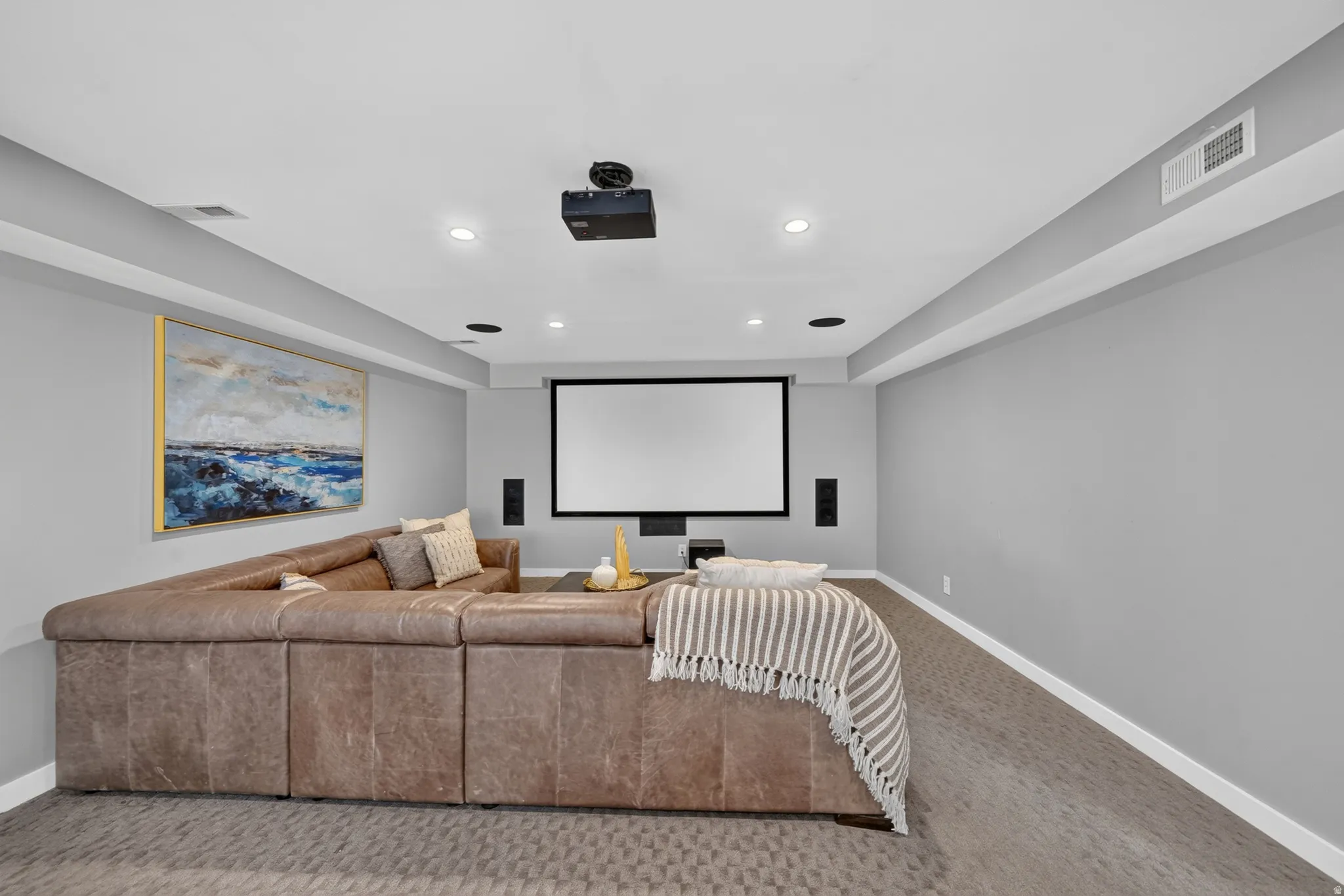 Dedicated media room featuring a large projection screen, recessed lighting, and wall-mounted speakers