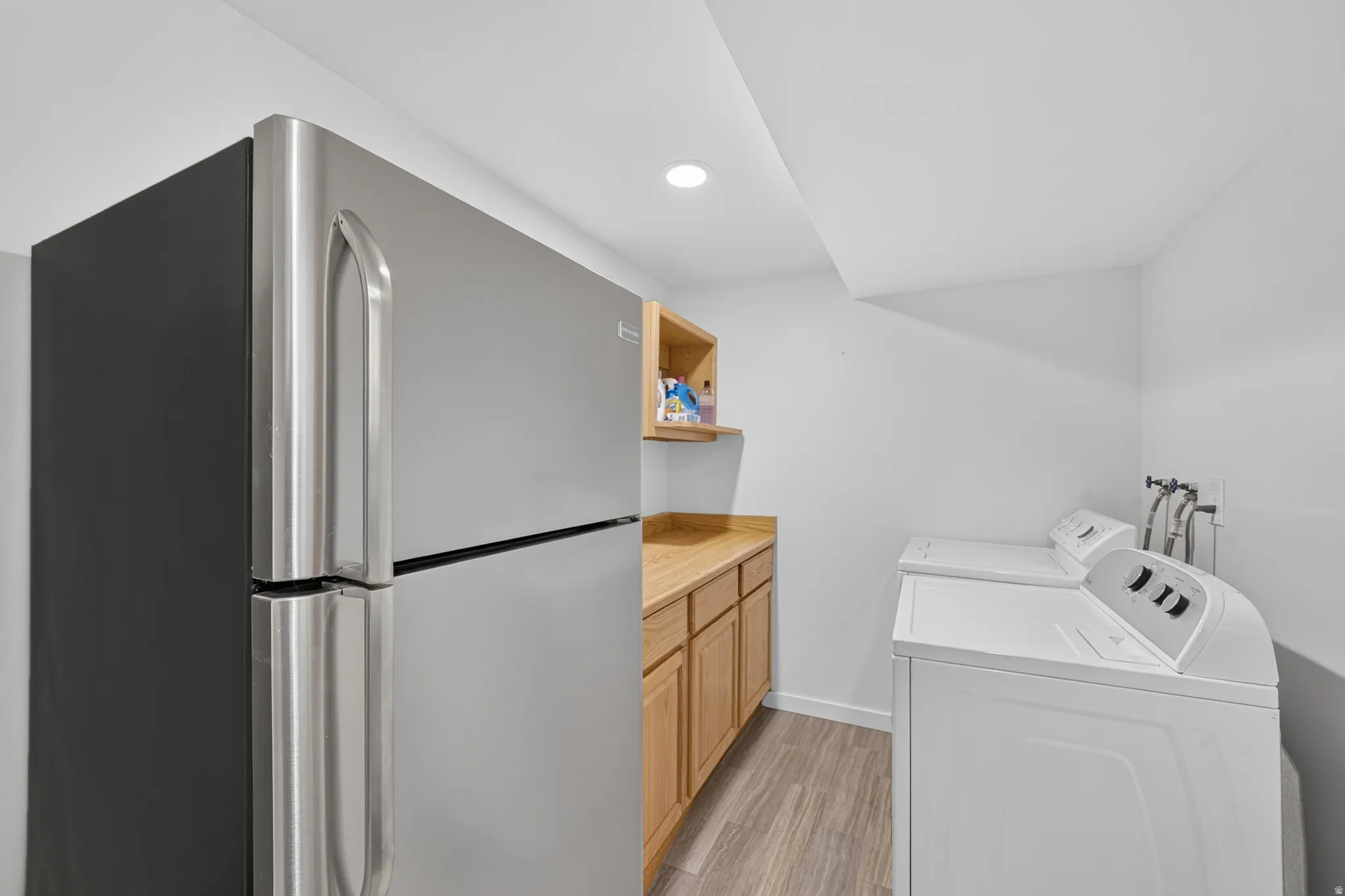 Utility space featuring a stainless steel refrigerator, light wood-finish cabinetry with a countertop, and wood-finish flooring